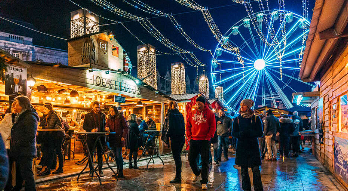 Vue nocturne du marché de Noël de Liège, avec des chalets illuminés et des visiteurs flânant sous les décorations lumineuses